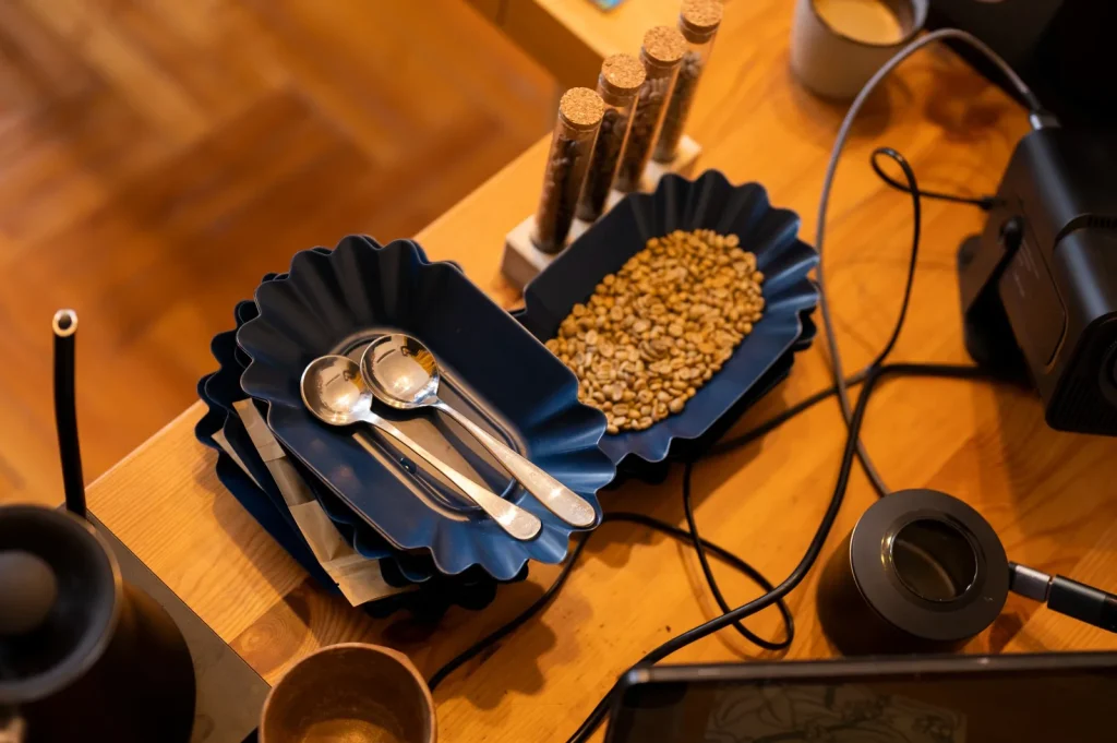 Green coffee beans on a blue tasting tray, with cupping spoons